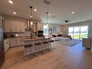 A modern open kitchen with sleek cabinetry, an island with seating, and a cozy living area opening to a bright backyard view.