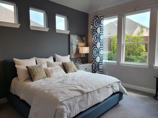 A cozy bedroom with a plush bed, patterned curtains, and modern lighting, featuring a large window view.