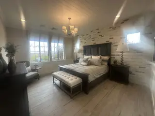 Cozy bedroom with brick accent wall, plush bedding, and warm lighting, featuring elegant wood furniture and large windows.