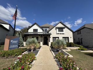 Street view A stunning white stone home with black accents and lush landscaping in Wolf Ranch by Coventry Homes (Georgetown, TX).