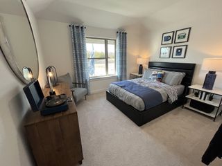 A cozy bedroom with a sleek black bed, modern decor, and a turntable on a wooden dresser. Plush carpet enhances the serene vibe.