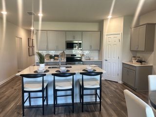 A modern kitchen with sleek gray cabinets, a white island, and stylish bar stools, featuring warm wood flooring.
