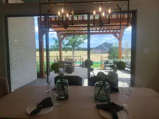A dining area with elegant table settings opens to a patio with wooden pergola and scenic views.