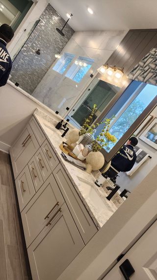 A modern bathroom featuring a double vanity with marble countertops, gold fixtures, and a spacious walk-in shower with intricate tilework.