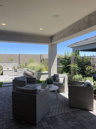 A cozy patio with wicker seating, lush greenery, and paver flooring, offering a serene outdoor retreat.