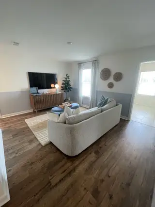 A cozy living room with elegant wood flooring, a plush sofa, and a modern entertainment setup. Neutral tones and stylish decor.