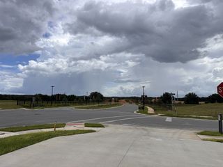 Scenic open roads with lush greenery in Waterstone by Taylor Morrison, Mascotte, FL, under a dramatic cloudy sky.