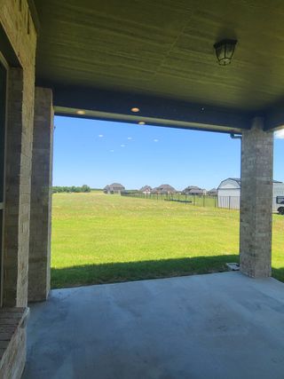 A covered patio with lush green field views, featuring brick pillars and cozy lighting for an inviting outdoor space.