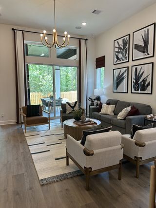 A modern living room with a gray sofa, chic armchairs, and wall art, opening to a patio with lush greenery.