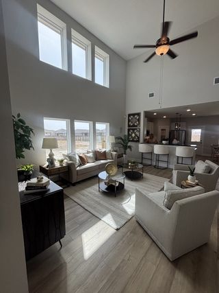 Model Home A stunning living space with soaring ceilings, abundant natural light from large windows, and a ceiling fan.