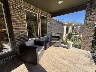 A close-up of the covered patio area, featuring modern outdoor furniture with black wicker chairs and a small side table. Large windows connect the patio to the home's interior.