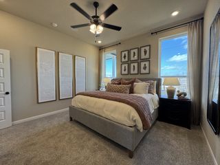 Model Home A cozy bedroom with neutral tones, plush bedding, modern artwork, and a ceiling fan for a comfortable ambiance.