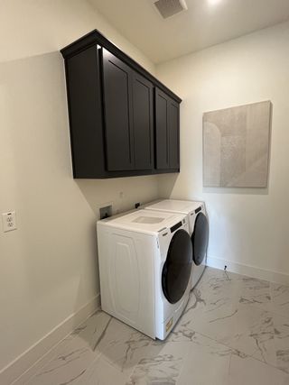 A modern laundry room with black cabinets and marble tile flooring in Solterra Texas by Shaddock Homes (Mesquite, TX).