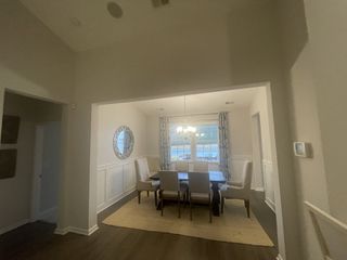 A dining room with elegant wainscoting, a large window, chandelier, and a spacious table with upholstered chairs.