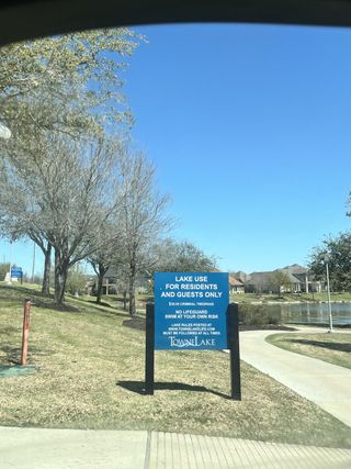 A community sign at Towne Lake in Cypress, TX, outlining lake use rules for residents and guests, with a glimpse of homes and a lake.