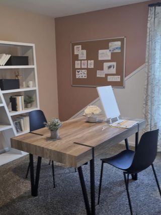 Model Home A cozy home office with a wooden desk, modern chairs, and a decorative bulletin board on a two-tone wall.