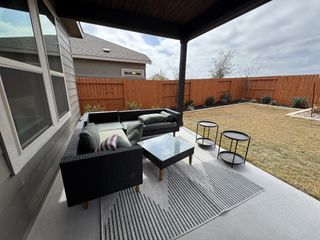 Model Home A cozy backyard patio with a modern outdoor sofa, glass table, and a well-maintained lawn.
