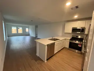 An open-concept kitchen and living area featuring white cabinetry, stainless steel appliances, and warm wood-style flooring.