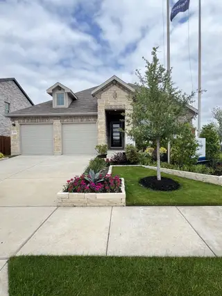 Street view A charming stone facade home with lush landscaping in Simpson Crossing - Signature Series by Meritage Homes (McKinney, TX).