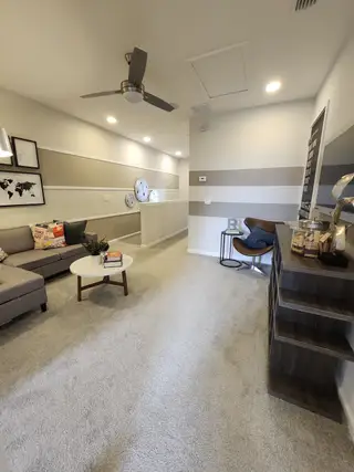 A modern lounge area with striped walls, cozy seating, and stylish decor, featuring a sleek ceiling fan and neutral tones.