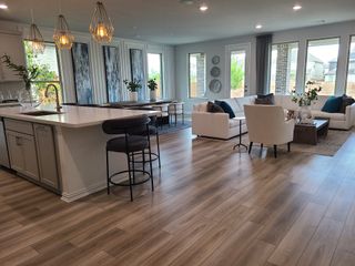 A spacious modern living area with wood flooring, elegant lighting, and cozy seating in a bright, open-concept design.