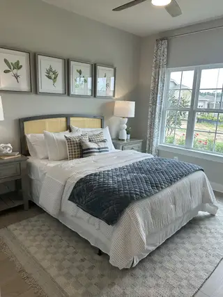 Model Home A cozy bedroom with botanical art, a plush bed, elegant nightstands, and a large window for natural light.