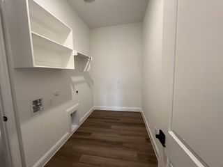 Model Home A bright laundry room with white shelving, wooden floors, and space for appliances.