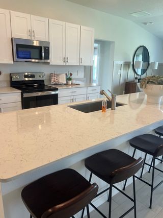 Model Home Modern kitchen featuring white cabinetry, stainless steel appliances, and a sleek island with bar seating and elegant decor.