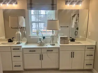 A spacious bathroom with dual sinks, elegant lighting, black fixtures, and a large window.