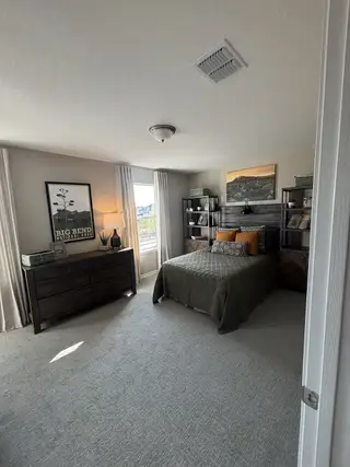 A cozy bedroom with a modern design, featuring a plush carpet, stylish artwork, and ample natural light.