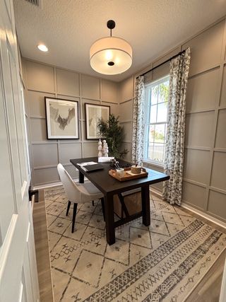 A cozy home office with paneled walls, a dark wooden desk, patterned rug, and elegant lighting.