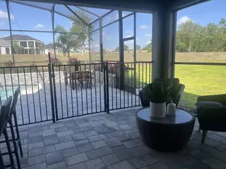 Model Home A cozy screened-in patio with outdoor seating, potted plants, and paving stones, overlooking a pool and green lawn.