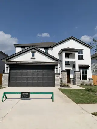 Street view Elegant white and stone-accented home with modern black garage in Morningstar by Saratoga Homes (Georgetown, TX).