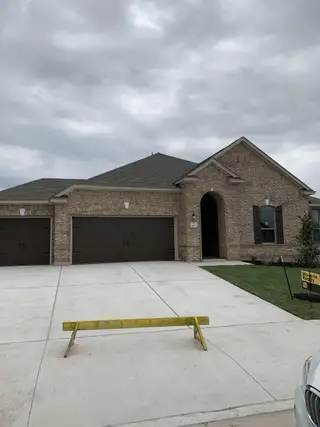 Street view A newly completed brick home in Salerno by KB Home (Round Rock, TX) features a three-car garage and a well-maintained front lawn, ready for move-in.