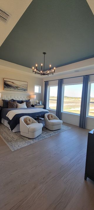 Model Home A spacious bedroom with elegant blue accents, cozy seating, and large windows offering scenic views.