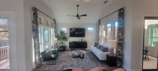 A bright living room with a sleek ceiling fan, modern furniture, large windows, and stylish curtains.