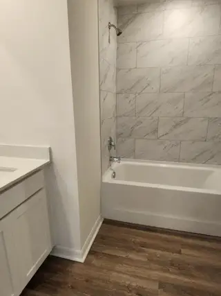 A sleek bathroom with a marble-tiled shower, white vanity, and wood flooring.