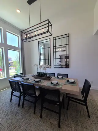 A modern dining room with a sleek table, black chairs, and large grid mirrors, bathed in natural light from expansive windows.