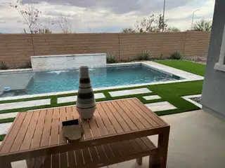 A serene backyard with a modern pool, sleek wooden table, and minimalist landscaping for ultimate relaxation.