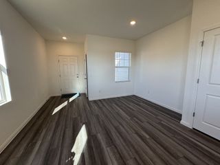 A bright room with wood flooring, white walls, and ample natural light from a window beside the door.