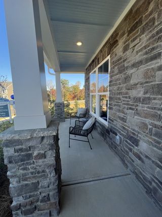 Model Home A cozy stone porch with black chairs and pillows, perfect for relaxation.