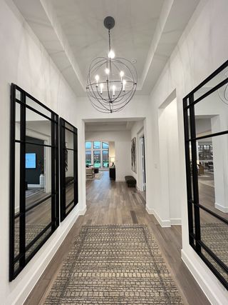 A bright hallway with modern lighting, mirrored walls, and a patterned rug leading to an open living area.