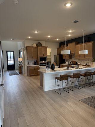 Model Home A modern kitchen with sleek wooden cabinetry, a large island featuring leather bar stools, and elegant pendant lighting.
