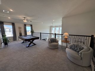 A spacious game room with a pool table, cozy armchairs, and ample natural light from large windows and elegant curtains.