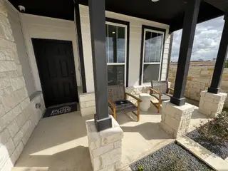 A cozy stone-accented patio with modern chairs and a black door welcomes you in Highcrest Meadow West by Tri Pointe Homes (Georgetown, TX).