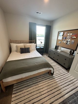 A cozy bedroom with a simple bed, striped rug, and a large corkboard for personal touches.