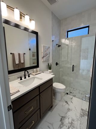 A sleek bathroom with a marble-tiled shower, gold fixtures, and a modern black-framed mirror.