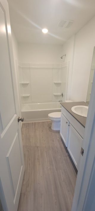 A bright bathroom featuring a shower-tub combo, sleek vanity, and light wood flooring.