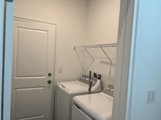 A compact laundry room with white appliances, wire shelving, and a simple design for efficient functionality.