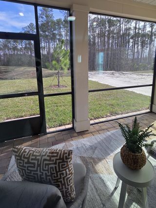 Model Home A cozy sunroom with wicker seating, decorative pillows, and a forest view through large screened windows.